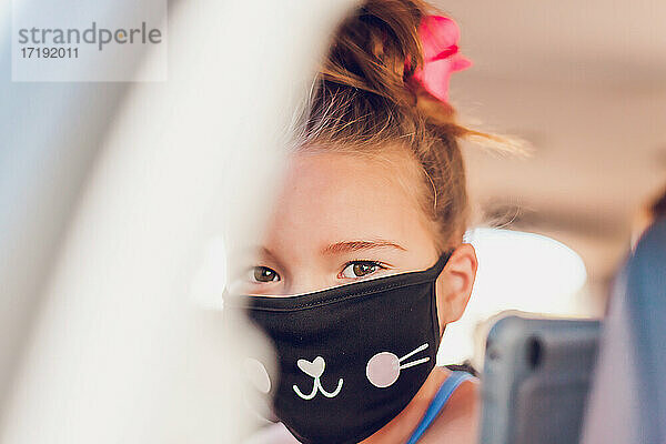 Junges Mädchen mit hübschen Augen trägt eine Katzenmaske in einem Auto.