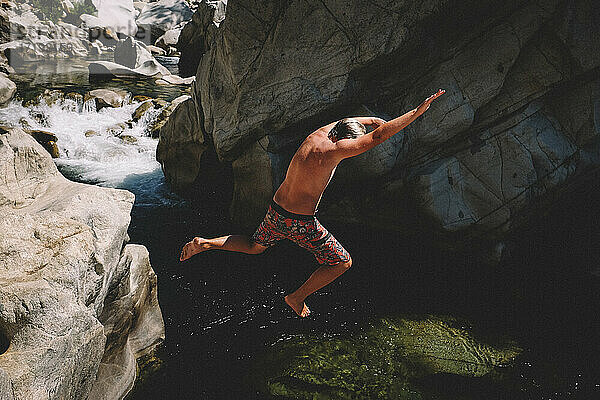 Junge in bunter Badehose springt von einer Klippe in einen schönen Fluss