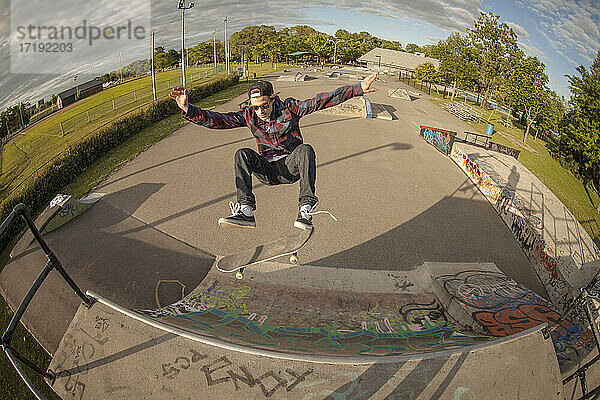 Mann auf Skateboard springt auf Rampe in Skatepark