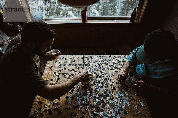 Zwei Männer arbeiten an einem Rätsel mit Fensterlicht in einer rustikalen Hütte
