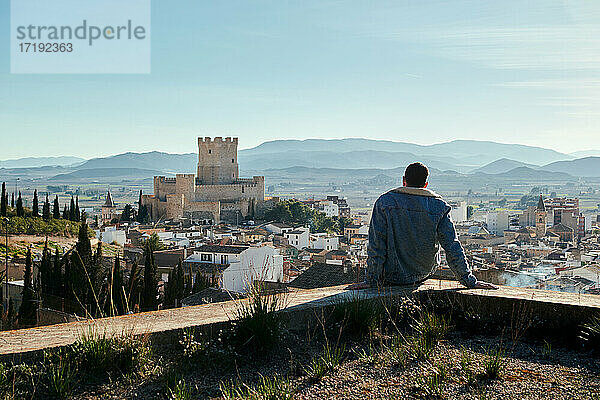 Mann sitzt auf einem Dach mit Blick auf die Burg einer Stadt in Spanien
