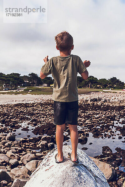 Junge auf dem Gipfel eines Felsens am Meer - mit dem Rücken zur Kamera.