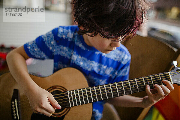Kleiner Junge spielt zärtlich auf der Veranda seines Hauses auf einer Akustikgitarre