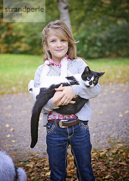 Junges blondes Mädchen hält eine schwarze und weiße Katze im Freien