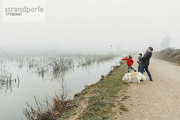 Vater und zwei Söhne mit Hund  die an einem nebligen Tag Steine in einen See werfen