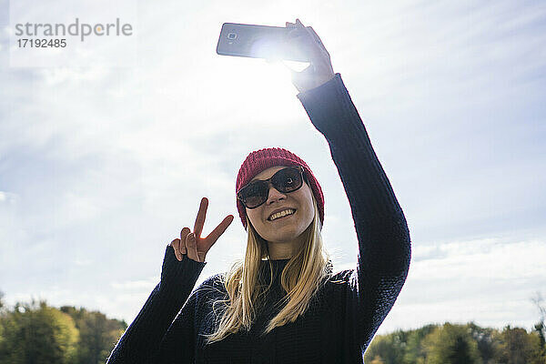 Kanadische junge Frau im Park  die ein Smartphone für ein Selfie benutzt