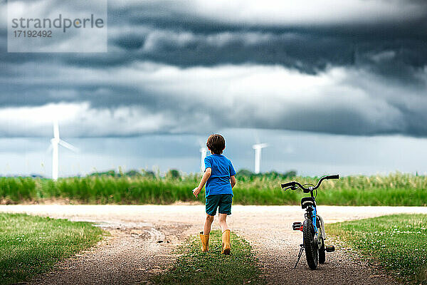 Junge mit Fahrrad beobachtet Sturmwolken über einem Windpark in Iowa