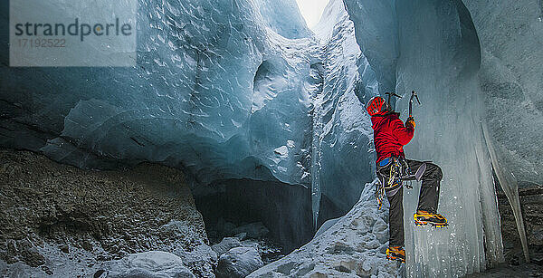 Mann klettert auf Eiszapfen in einer Gletscherhöhle in Island