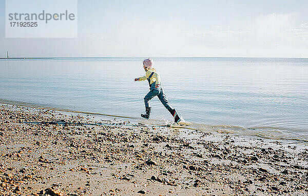 junges Mädchen  das am Strand in der Sonne fröhlich durch das Meer läuft