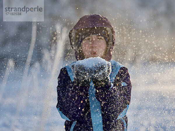 Porträt eines Mädchens  das im Winter Schneeflocken in die Kamera bläst  Fokus auf Schnee