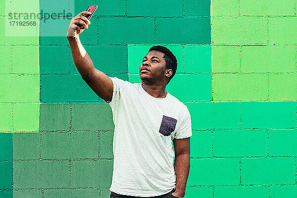 Schwarzer afroamerikanischer Junge auf grünem Hintergrund  der ein Selfie mit seinem Mobiltelefon macht.