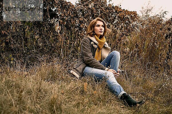 Porträt einer jungen Frau mit Pullover  die im Gras sitzt