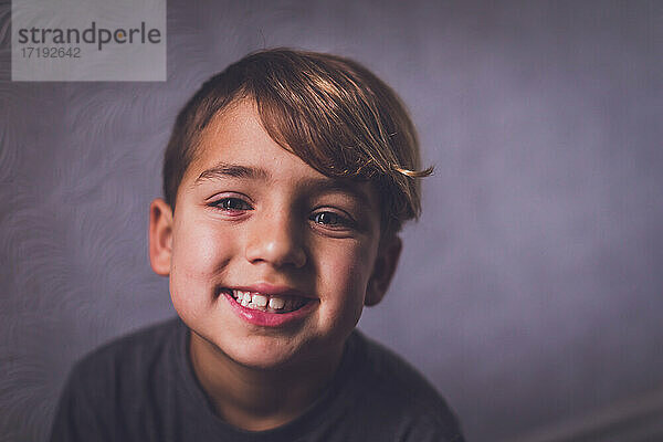 Ein lächelnder Junge mit haselnussbraunen Augen schaut in die Kamera.