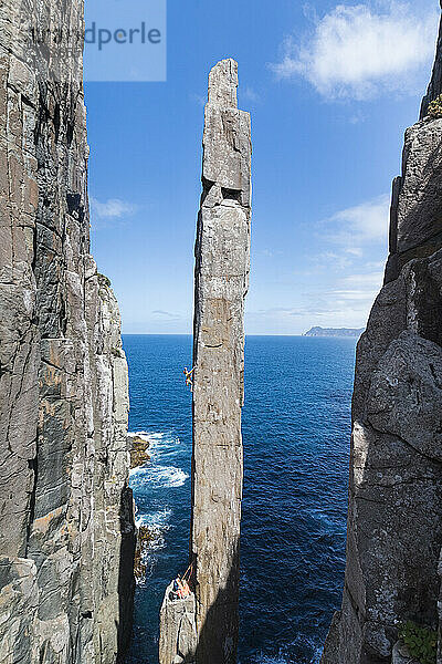 Eine Bergsteigerin hält sich an der Kante des Totem Pole fest  einem freistehenden  exponierten Meerstapel  der im Cape Hauy  Tasman National Park  Tasmanien  Australien  aus dem Meer auftaucht.