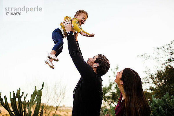 Vater hebt lächelnde Tochter hoch  während Mutter in San Diego zusieht