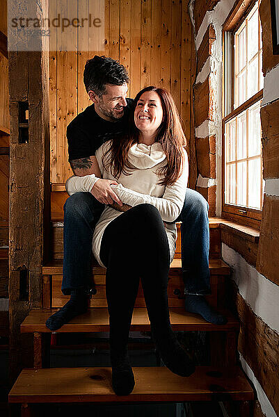 Glückliches Paar sitzt zusammen auf einer Treppe in einem rustikalen Blockhaus.