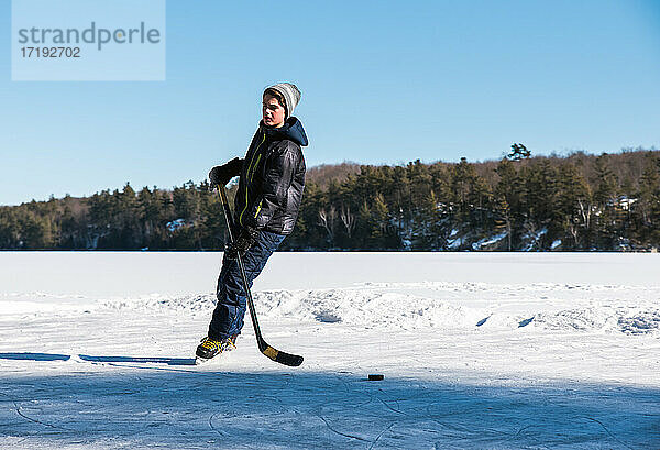 Ein Jugendlicher spielt Hockey auf einer Eisbahn auf einem zugefrorenen See in Kanada.