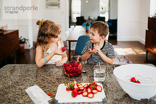 Bruder und Schwester teilen sich frisch geschnittene Erdbeeren an der Kücheninsel