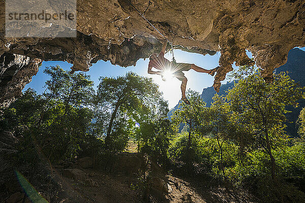 Mann klettert auf überhängendem Kalksteinfelsen in Laos