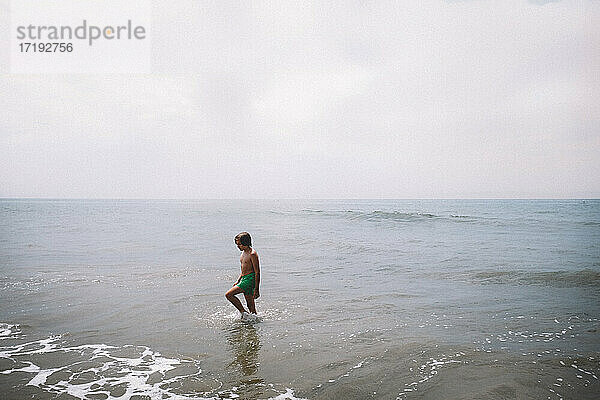 Junge  der an einem kalifornischen Strand durch seichtes Wasser schreitet