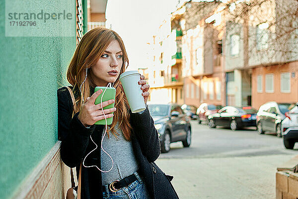 Geschäftsfrau hält eine Kaffeetasse  während sie auf ihr Telefon schaut