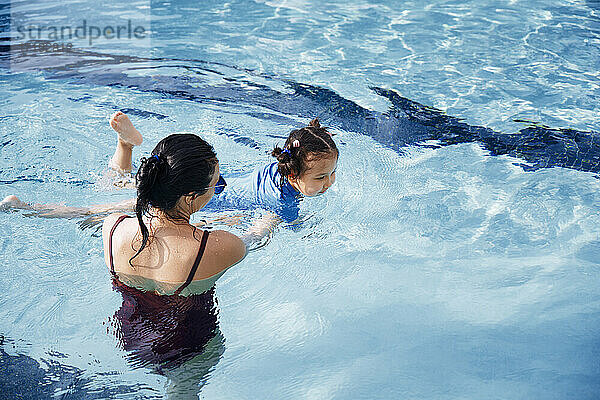 Mutter  die ihrer Tochter beim Schwimmen im Schwimmbad hilft