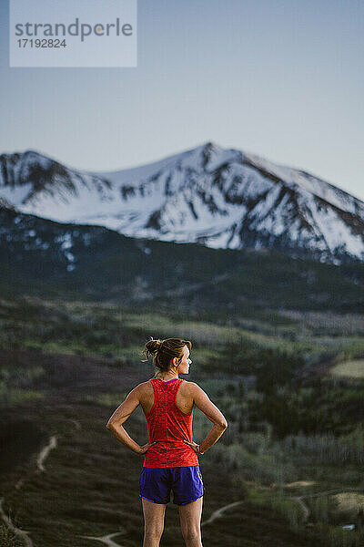 Junge Frau blickt beim Trailrunning in der Morgendämmerung auf die Berge