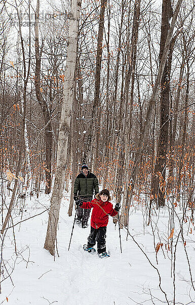 Kleiner Junge geht mit seinem Vater an einem verschneiten Wintertag im Wald Schneeschuhwandern.