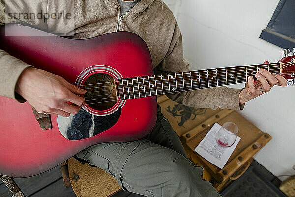 Nahaufnahme eines Mannes  der eine rote akustische Gitarre mit einem leeren Weinglas spielt
