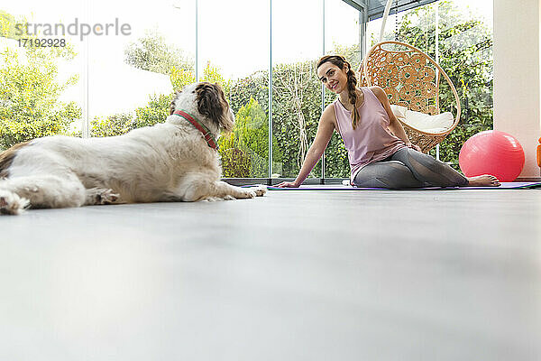 Frau in Zöpfen mit ihrem Hund macht Yoga  Fitness zu Hause
