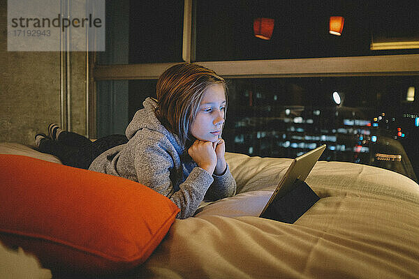 Tween am iPad am Abend. Lichter der Stadt durch das Fenster