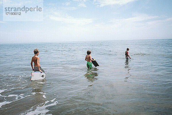 Drei Jungen stürzen sich mit Boogie Boards in den Ozean