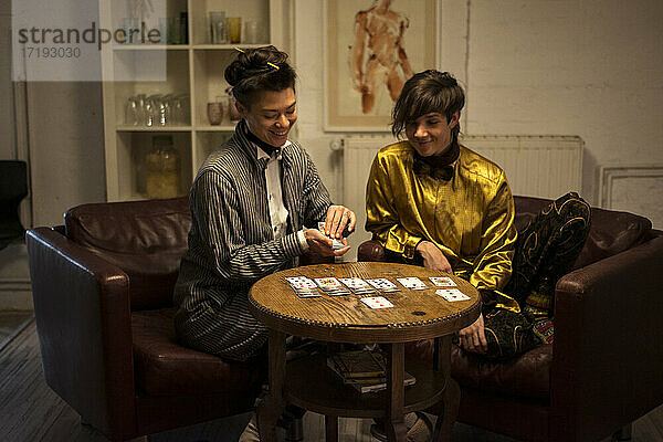 Freunde spielen Karten bei einer Dinnerparty zu Hause auf Sesseln und lachen