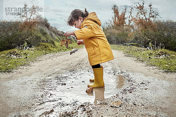 Ein 2-jähriges Mädchen spielt mit einer Schlammpfütze