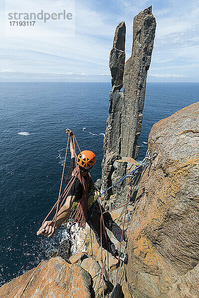 Ein männlicher Abenteurer rollt das Seil auf  während er seine nächste Herausforderung ins Visier nimmt: zwei freistehende Felspfeiler  die an den Klippen von Cape Raoul in Tasmanien  Australien  aus dem Meer ragen.