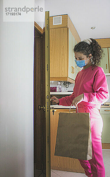 Frau mit Maske und rosa Trainingsanzug  die die Tür öffnet und eine Bestellung aufnimmt