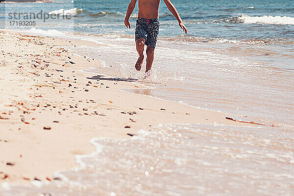 Unterkörper - Junge läuft am Strand.
