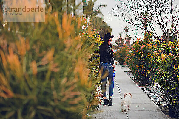 Junge Frau geht mit ihrem kleinen Hund in einer städtischen Umgebung spazieren.