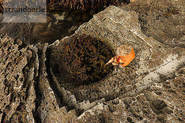 Blick von oben auf ein Kind  das einen runden Felspool in Neuseeland erkundet