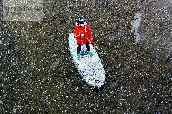 Hohe Winkel Ansicht der Frau Paddleboarding auf Fluss bei Schneefall