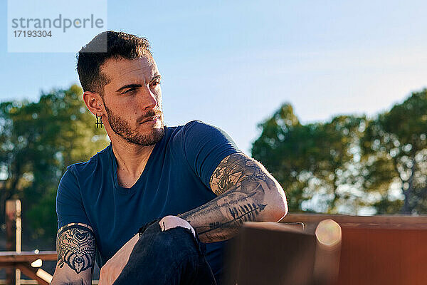 Attraktiver Mann mit Tattoos sitzt auf einer Bank