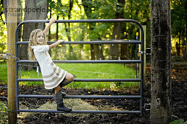 Kleines blondes Mädchen klettert auf dem Bauernhof über ein Tor.
