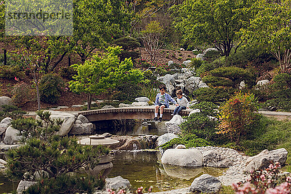 Zwei Jungen sitzen auf einer Brücke im japanischen Stil über einen Bach.