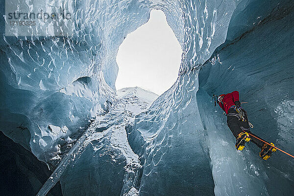 Mann klettert auf Eiszapfen in einer Gletscherhöhle in Island