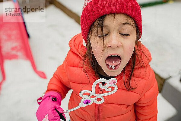 Junges Mädchen probiert Schnee und hält Spielzeugstab an einem Wintertag