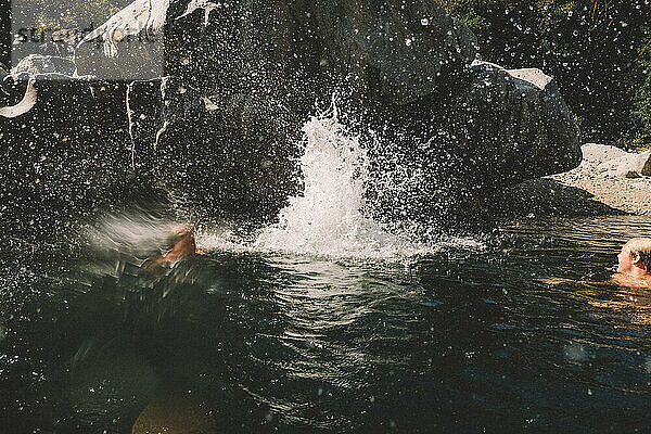 Große Spritzer und Wasserspritzer von Jungen  die in ein Schwimmloch springen