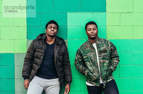 Porträt von zwei jungen schwarzen afroamerikanischen Jungen  die sich an eine grüne Wand lehnen.