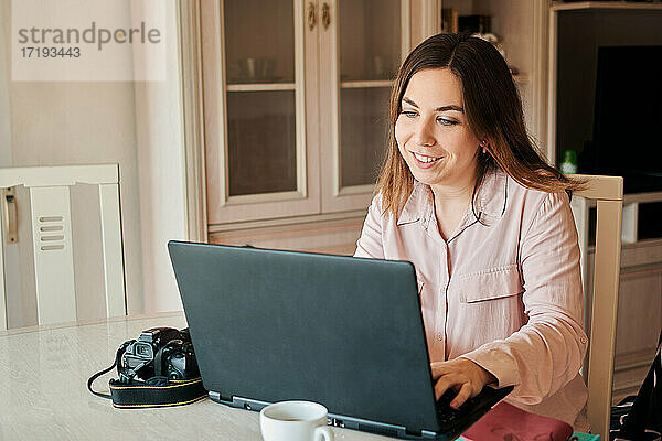 Junge Frau arbeitet von zu Hause aus an ihrem Laptop