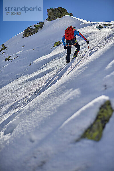 Ein Mann besteigt an einem sonnigen Tag einen verschneiten Berg in Devero  Italien.