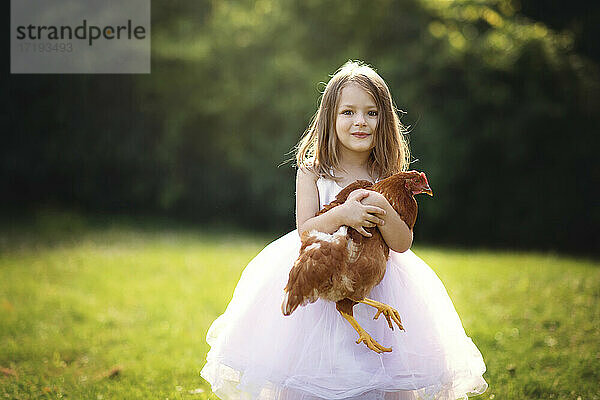 Niedliches kleines Mädchen hält ein Huhn im Freien im Gegenlicht.